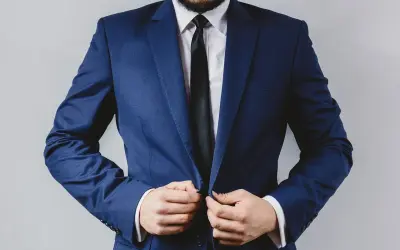 Mężczyzna w granatowym garniturze, białej koszuli i czarnym krawacie zapina marynarkę.