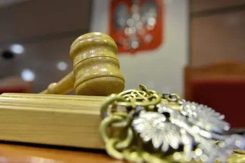 Młotek sędziowski i łańcuch z orłem na tle godła Polski.