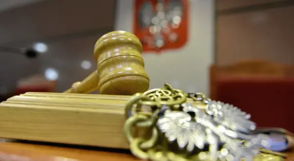 Młotek sędziowski i łańcuch z orłem na tle godła Polski.