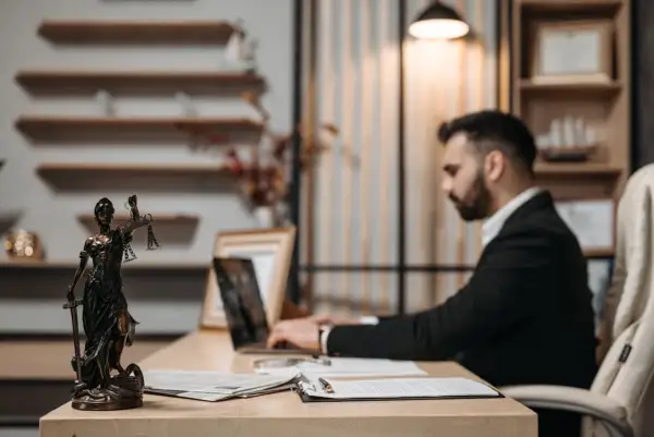 Figurka Temidy i prawnik pracujący przy laptopie w biurze.